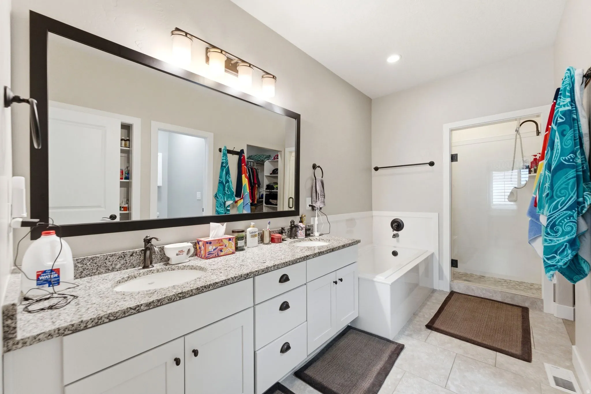Full bath featuring double vanity, a garden tub, a shower stall, a spacious closet, and light tile patterned floors