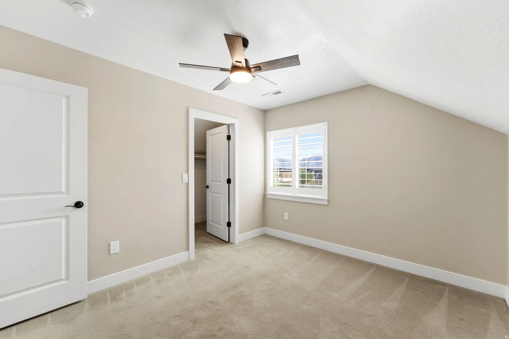 Unfurnished bedroom with a walk in closet, lofted ceiling, light colored carpet, and ceiling fan