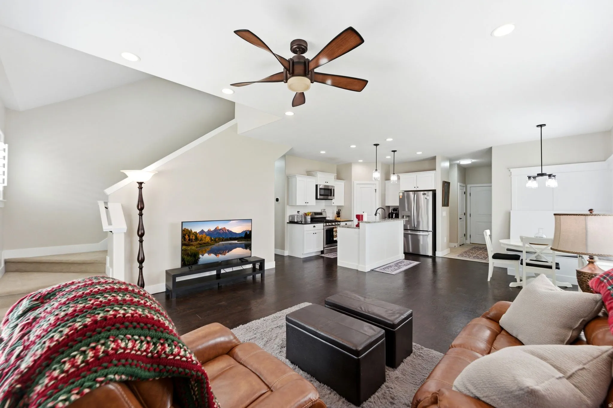 Living area with a ceiling fan, dark wood-style flooring, and hanging lights