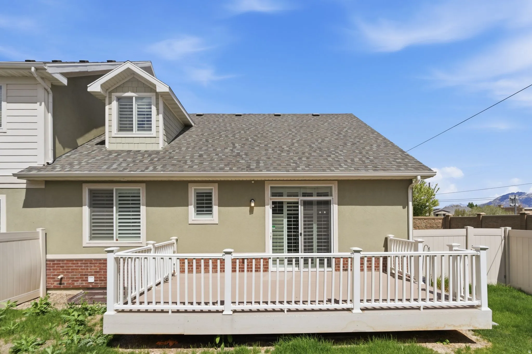 Back of property with a shingled roof, a deck, brick siding, and stucco siding