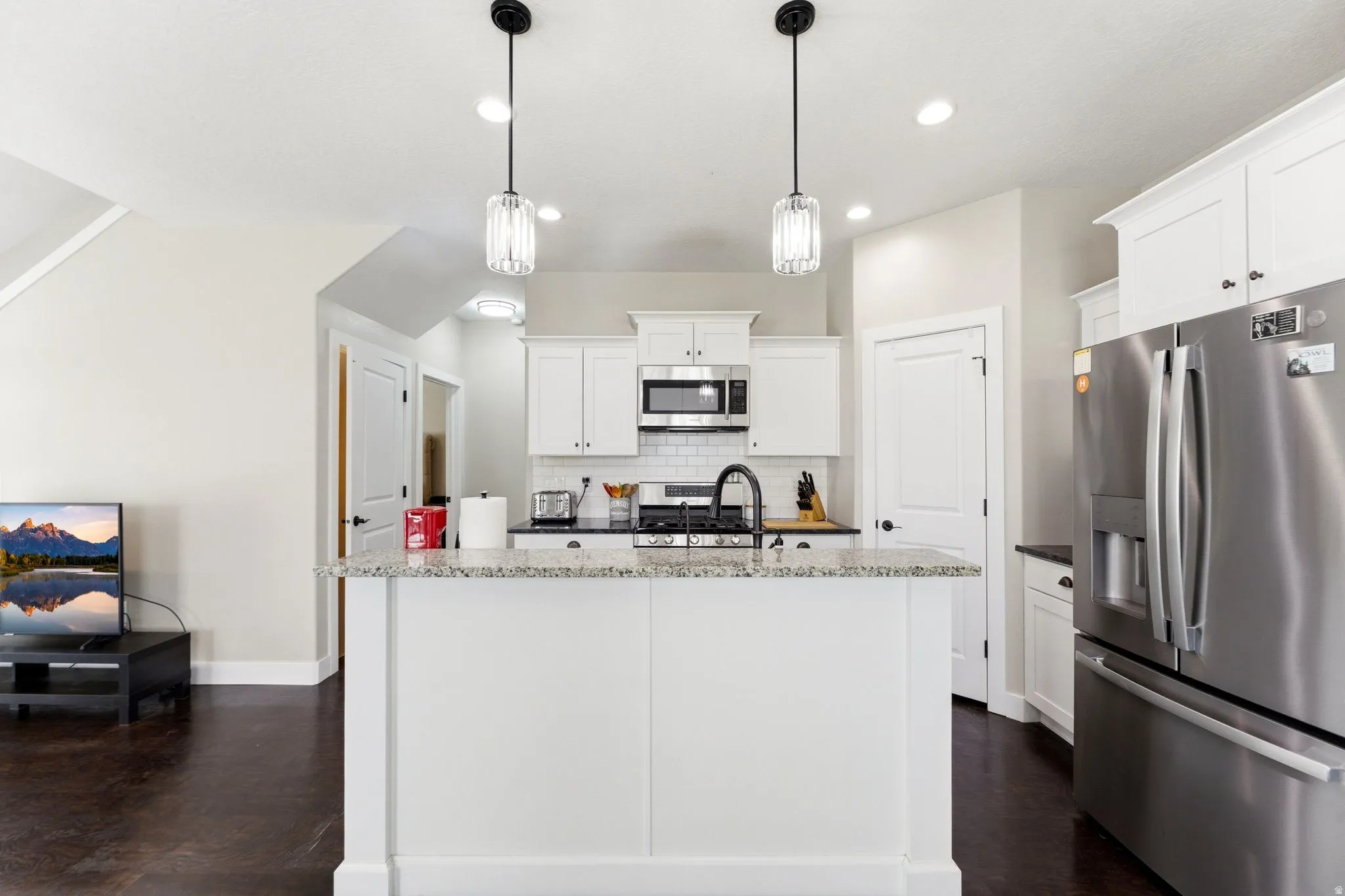 Kitchen with stainless steel appliances, white cabinetry, dark stone countertops, and a kitchen island with sink