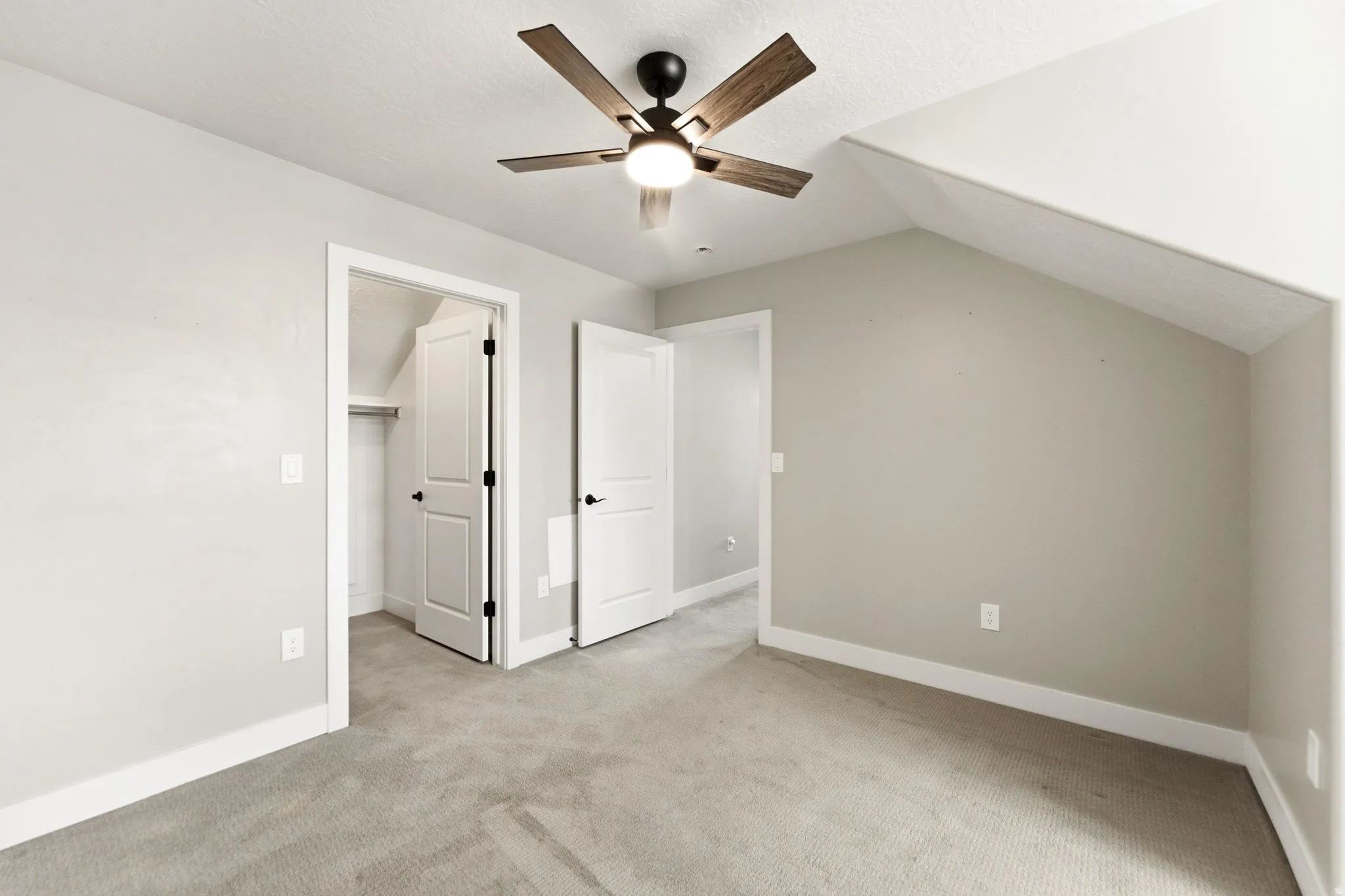 Unfurnished bedroom with a walk in closet, light colored carpet, and a ceiling fan
