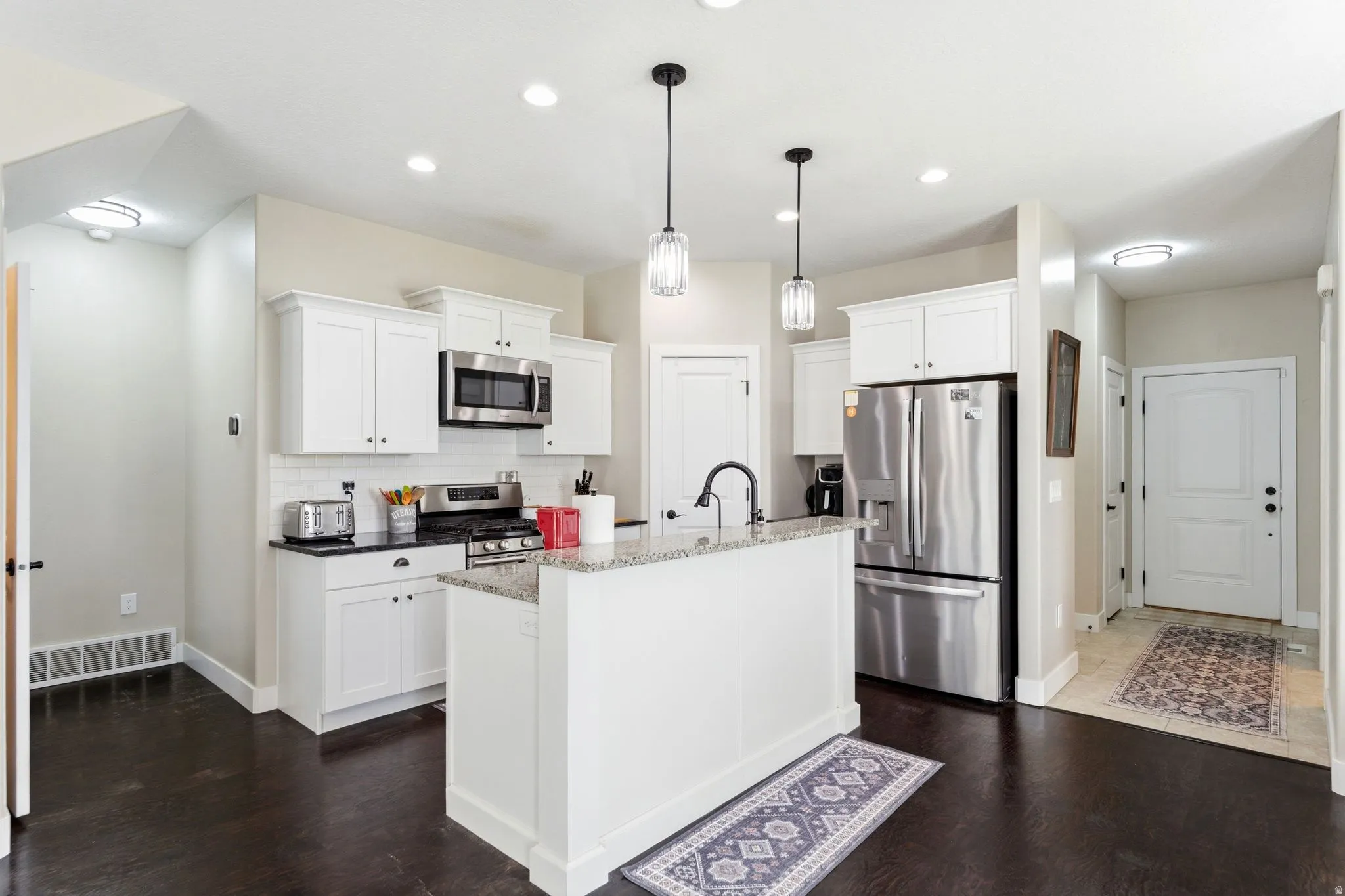 Kitchen featuring white cabinets, stainless steel appliances, dark stone countertops, and pendant lighting