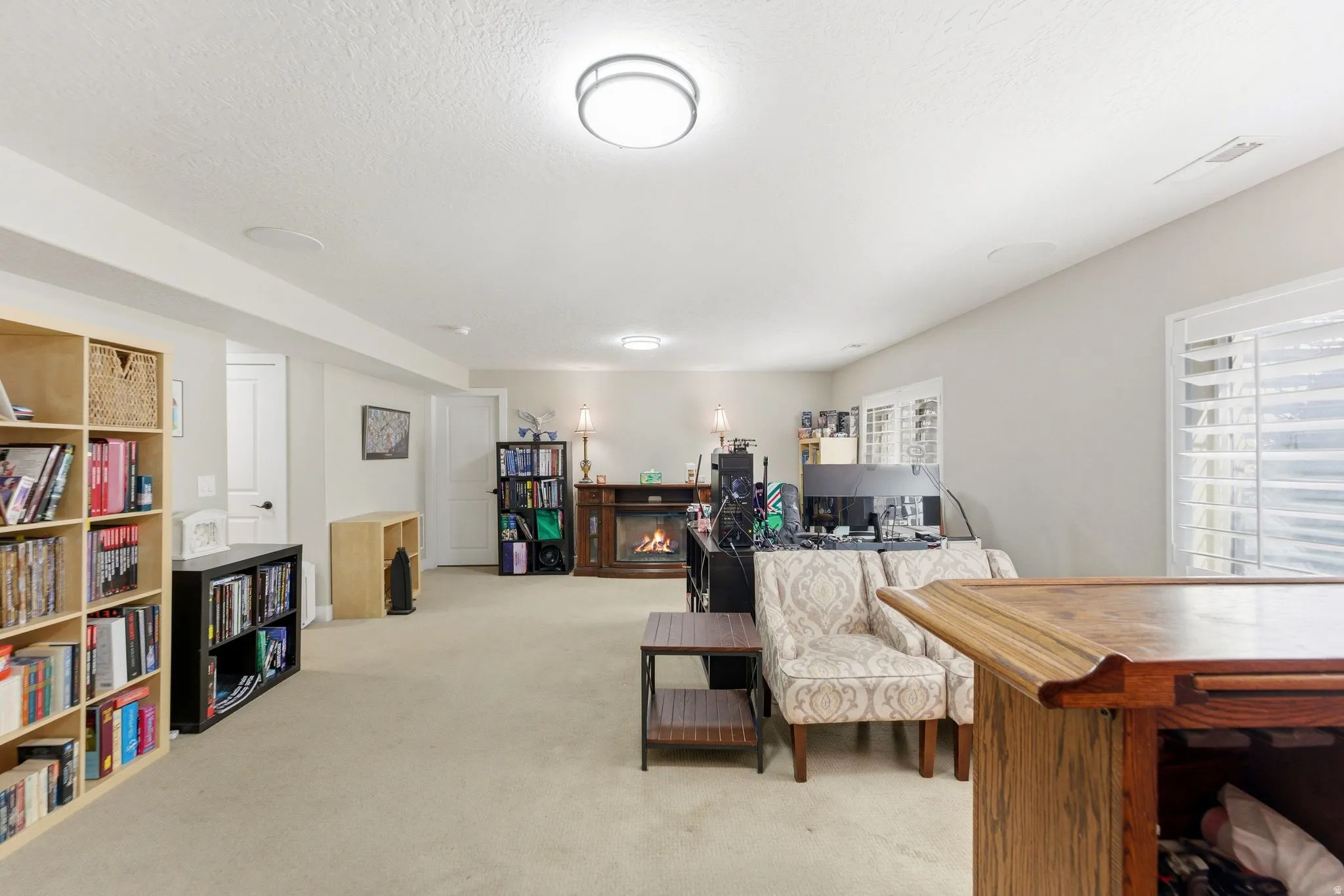Office with light colored carpet, a lit fireplace, and a textured ceiling