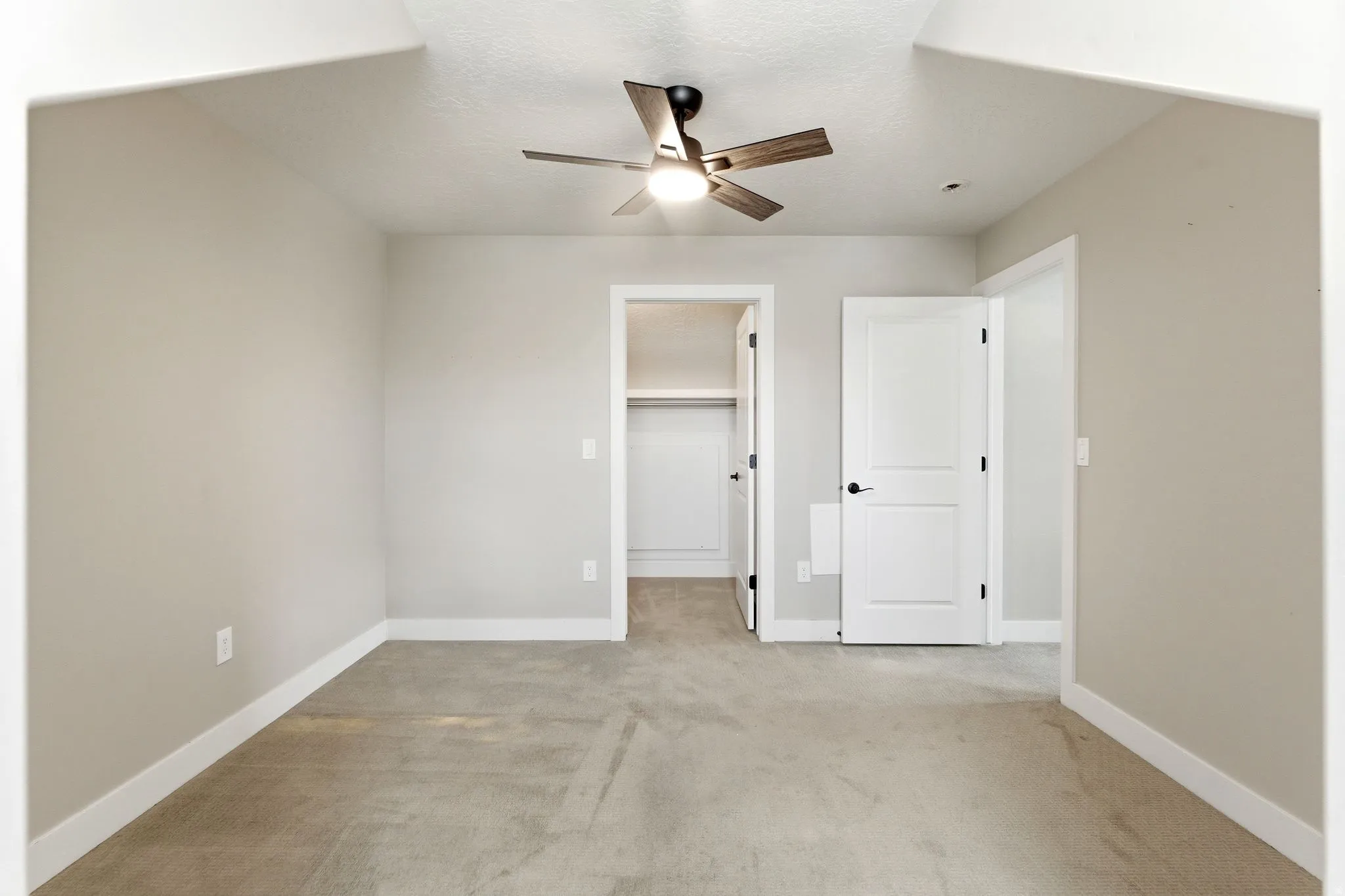 Unfurnished bedroom featuring a spacious closet, light carpet, and ceiling fan