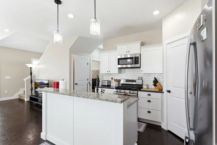 Kitchen with stainless steel appliances, white cabinets, a kitchen island with sink, backsplash, and decorative light fixtures