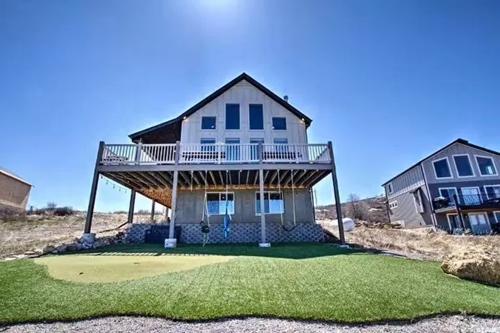 Back of house with a deck, a lawn, and a putting green