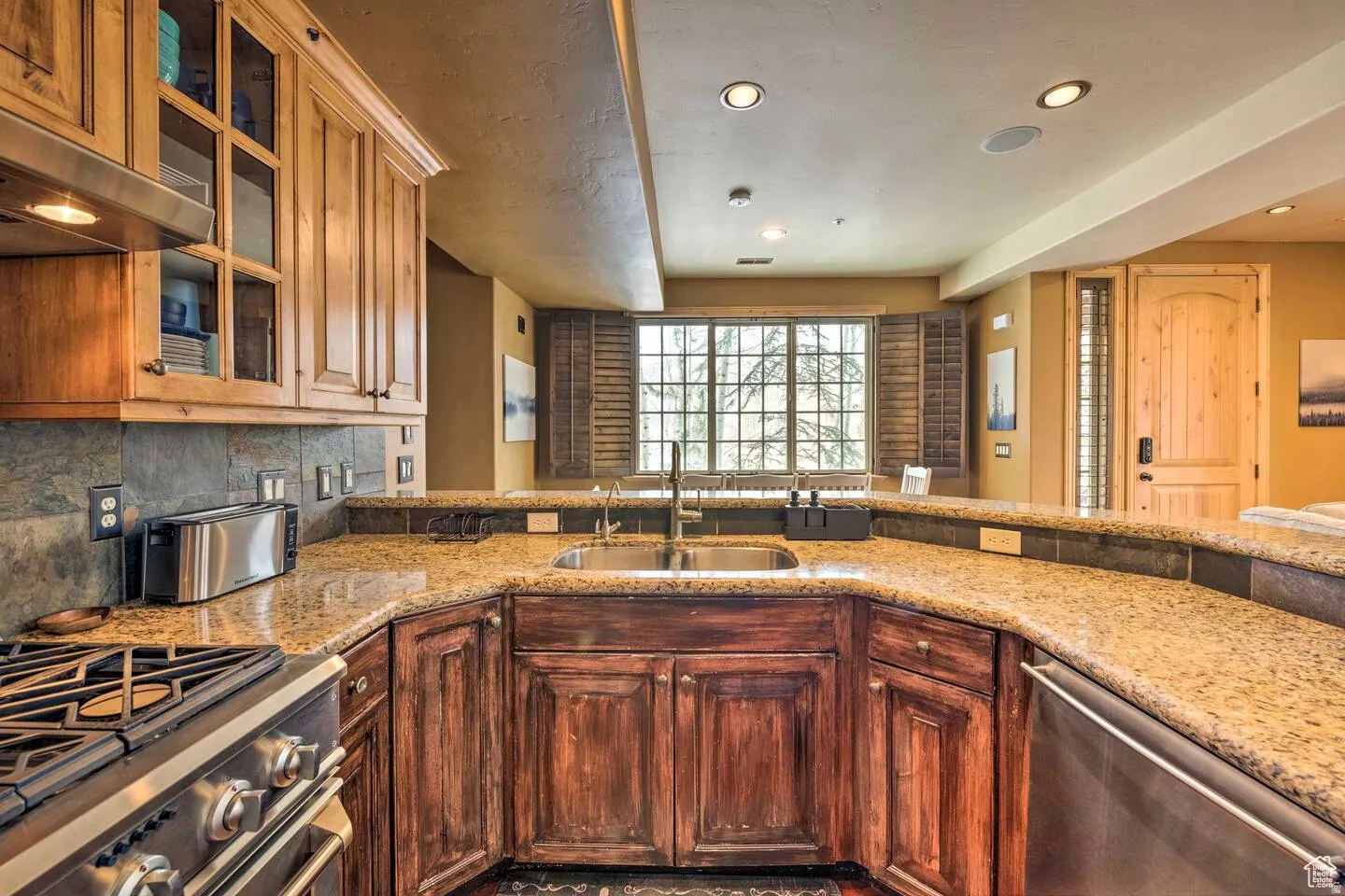 Kitchen with stainless steel appliances, glass fronted cabinets, light stone countertops, recessed lighting, and extractor fan