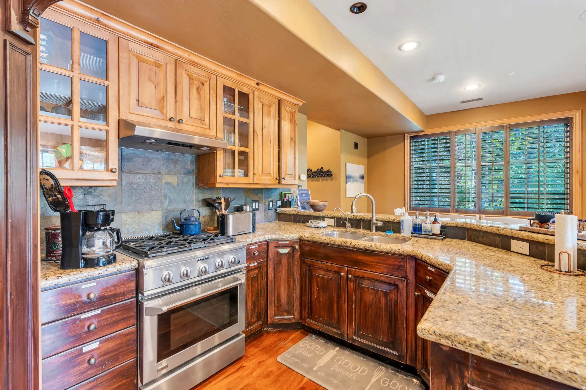 Kitchen with stainless steel range with gas cooktop, glass fronted cabinets, light stone countertops, decorative backsplash, and light wood-style floors