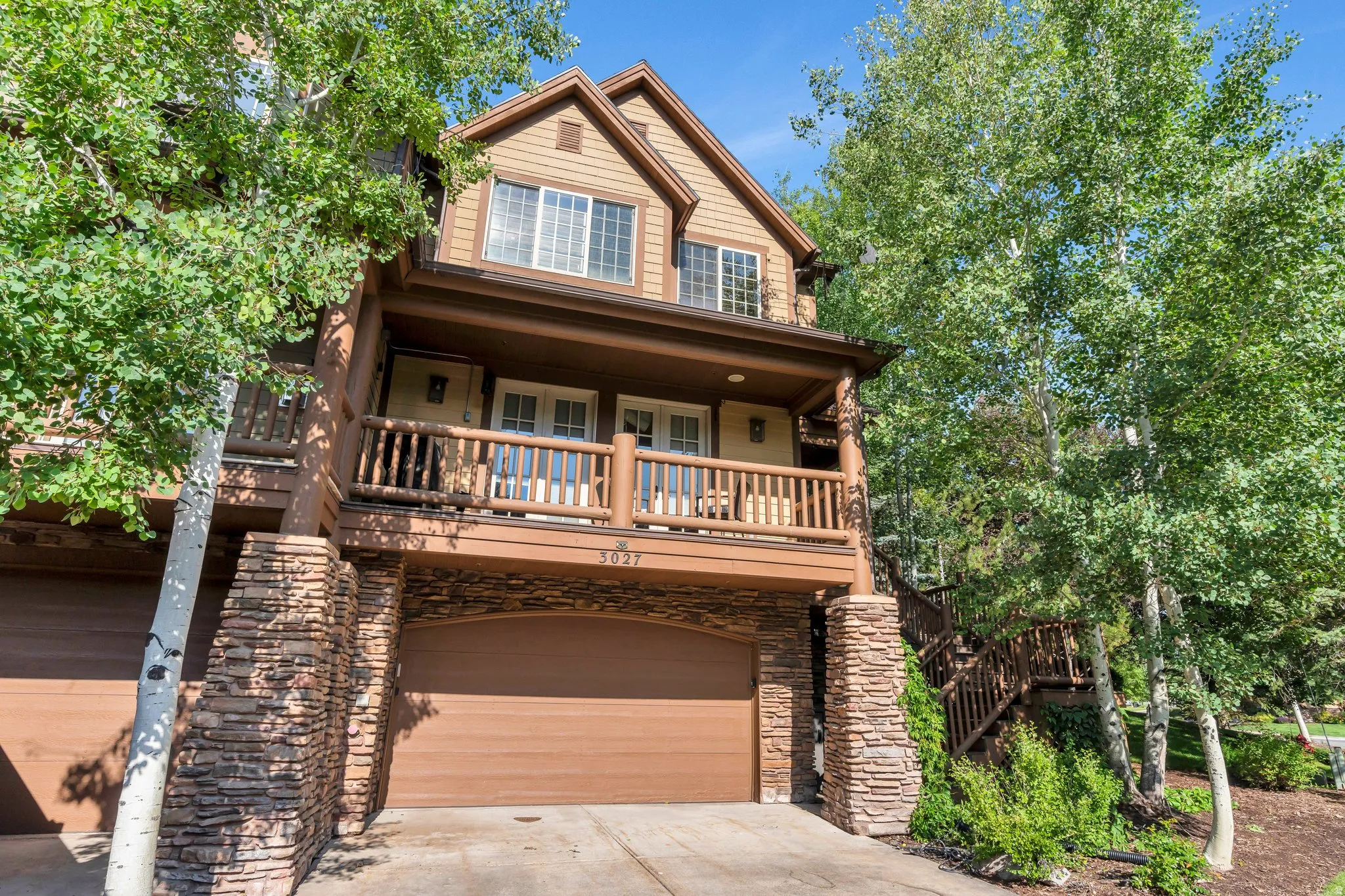 View of front of house with stone siding, driveway, an attached garage, and covered porch