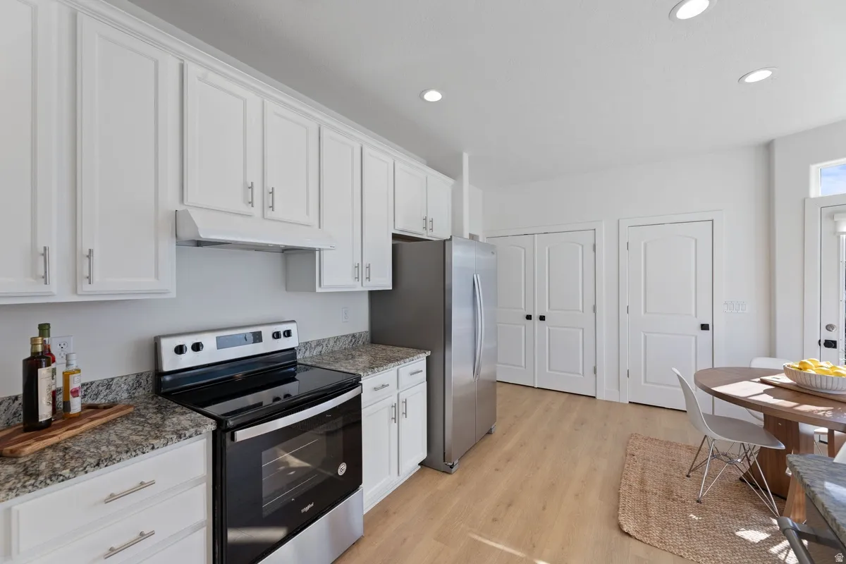 Kitchen featuring stainless steel appliances, white cabinetry, light wood-style floors, recessed lighting, and dark stone counters