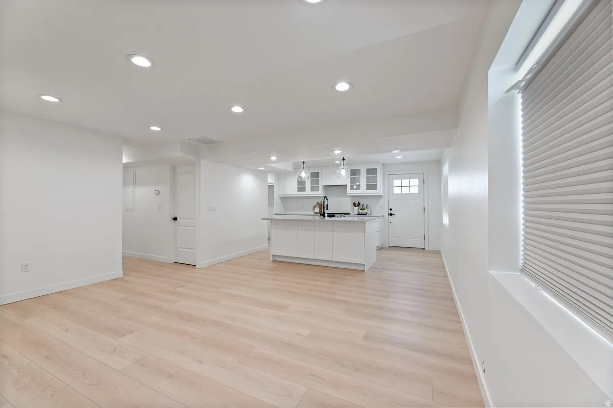Kitchen with glass insert cabinets, open floor plan, white cabinets, a kitchen island with sink, and light wood finished floors