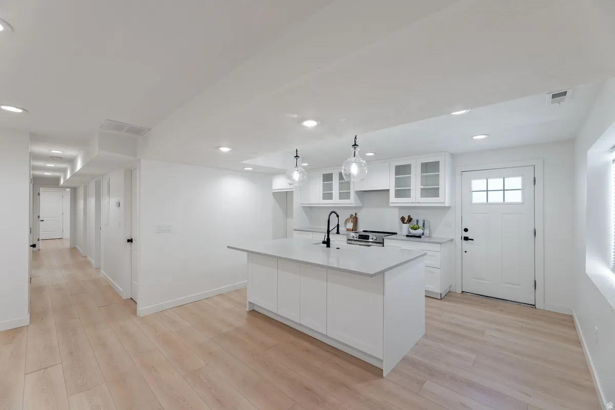 Kitchen with glass insert cabinets, white cabinets, an island with sink, and light wood-type flooring