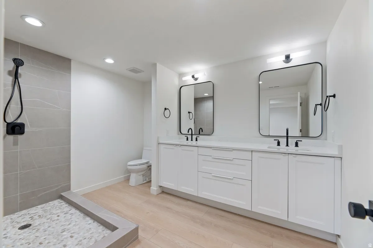 Full bath with double vanity, light wood-type flooring, a walk in shower, and recessed lighting