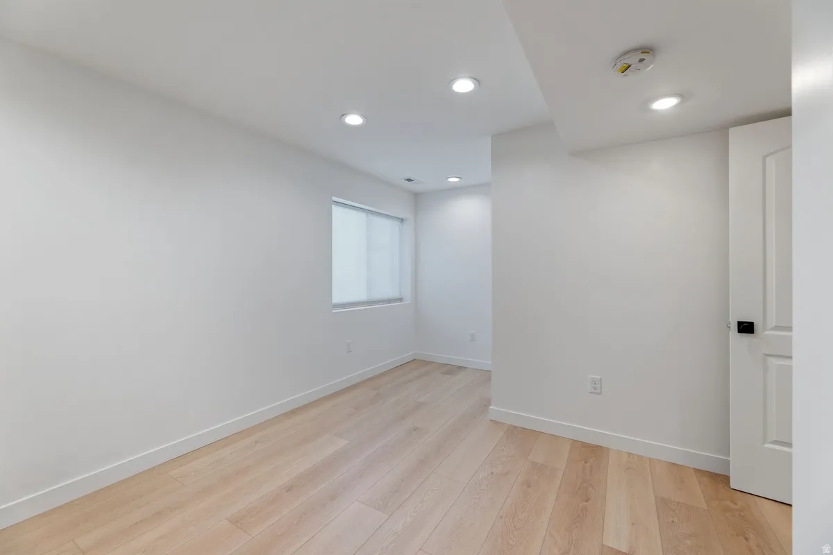 Empty room featuring light wood-style floors, recessed lighting, and a smoke detector