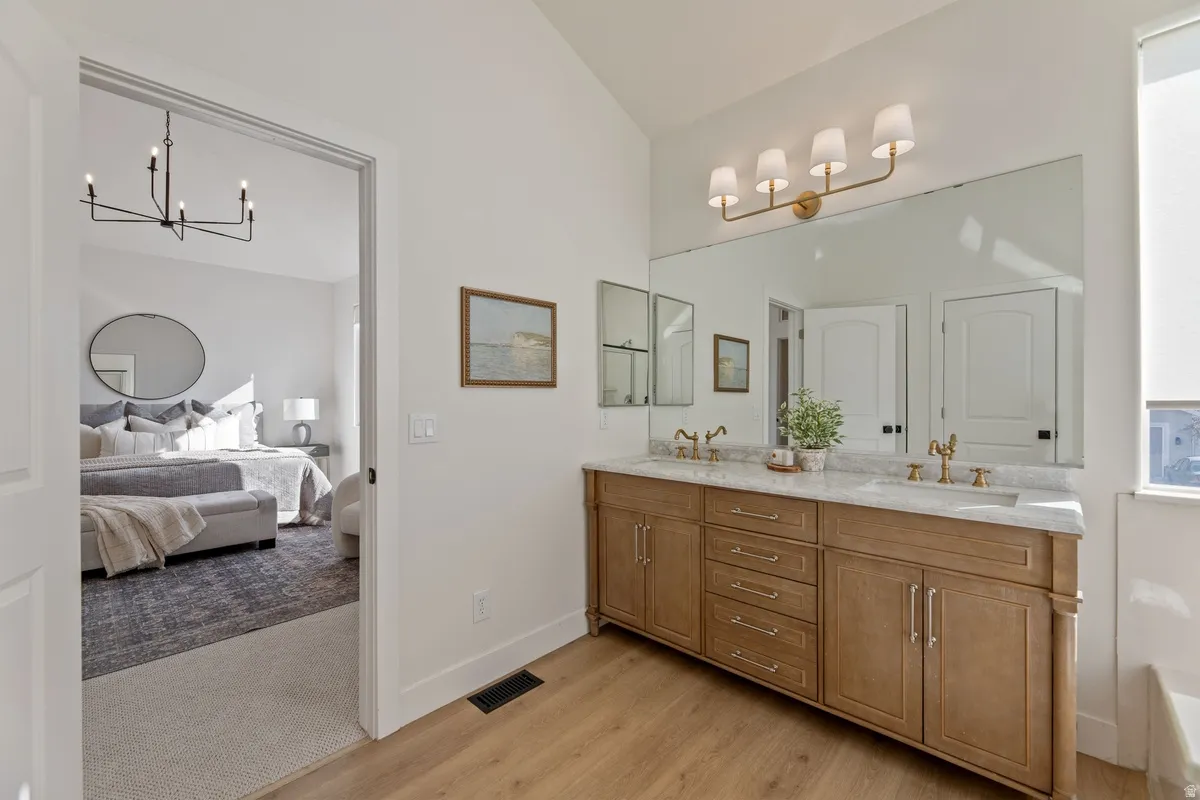 Full bathroom with ensuite bath, double vanity, hanging lights, lofted ceiling, and light wood-style flooring