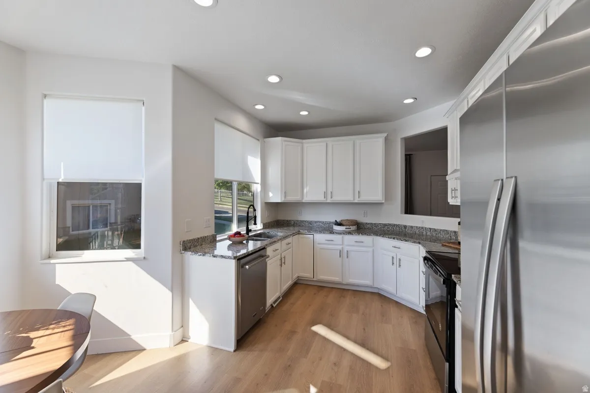 Kitchen featuring stainless steel appliances, white cabinets, dark stone counters, light wood-type flooring, and recessed lighting