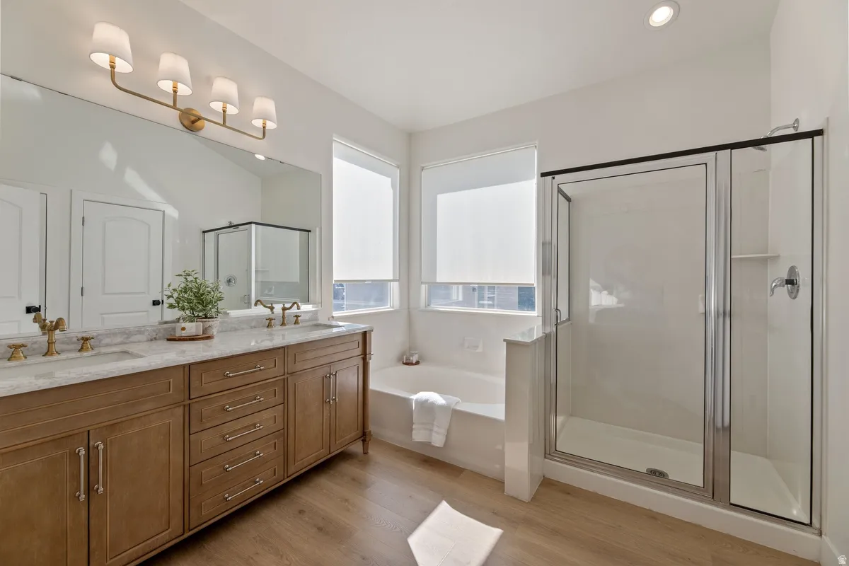 Bathroom with a stall shower, double vanity, light wood-style flooring, a bath, and recessed lighting