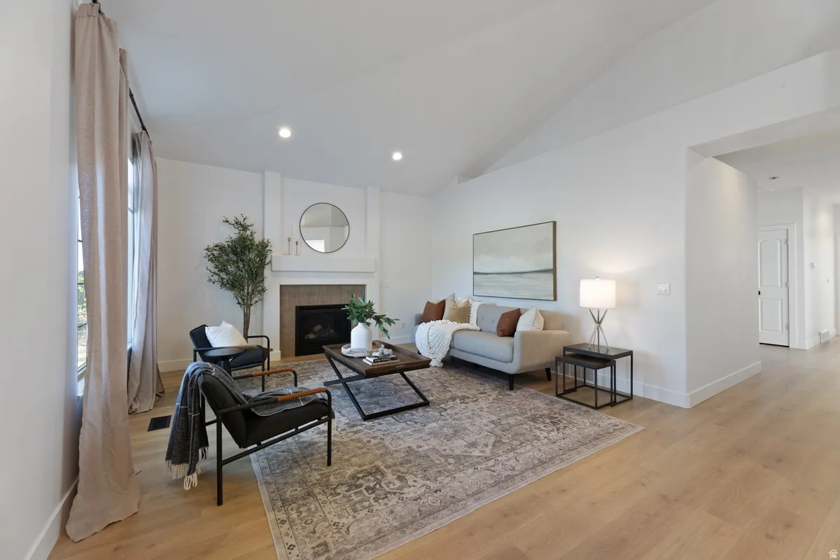 Living area with light wood-style floors, vaulted ceiling, a tiled fireplace, and recessed lighting