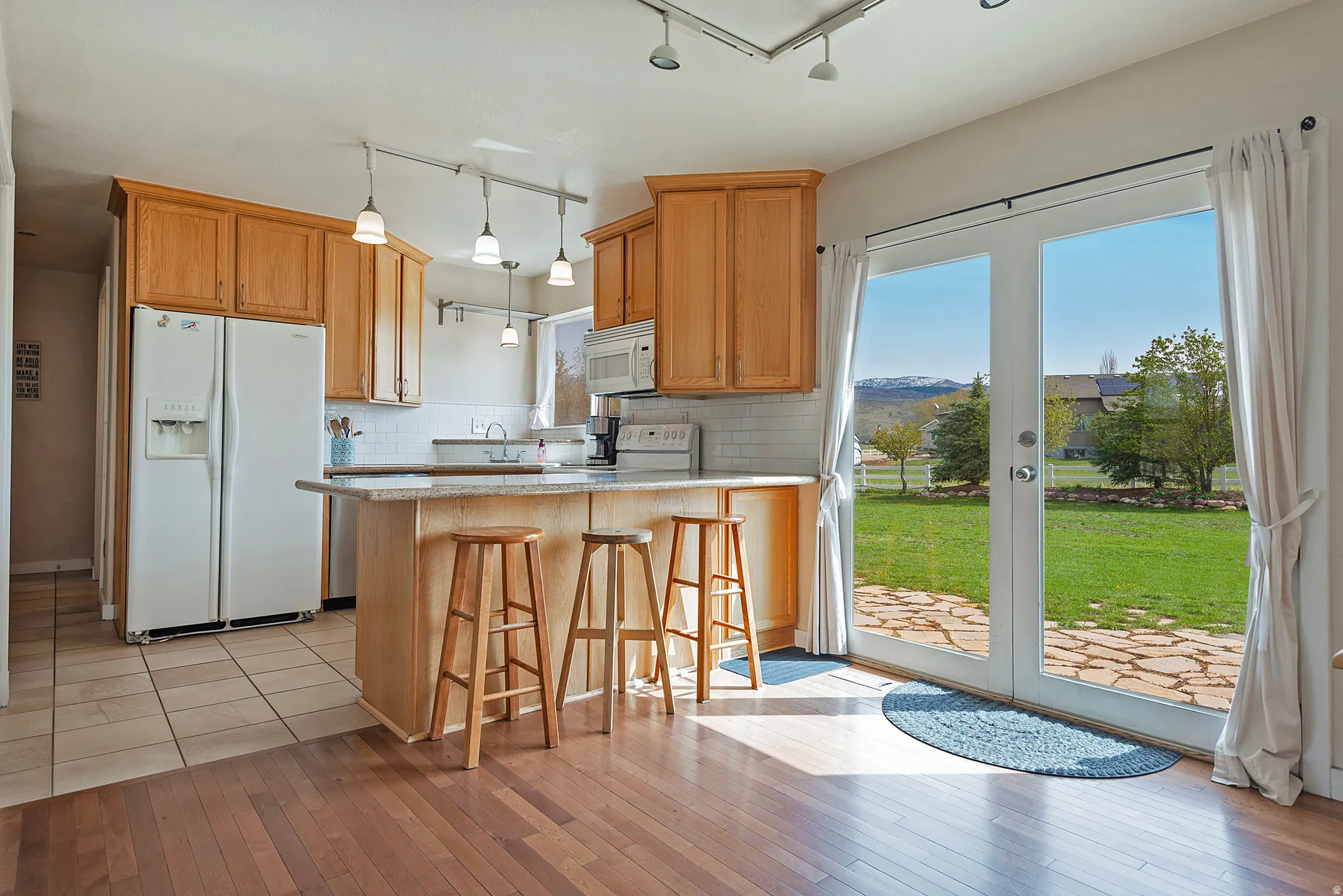 Kitchen with white appliances, a kitchen bar, a peninsula, rail lighting, and tasteful backsplash