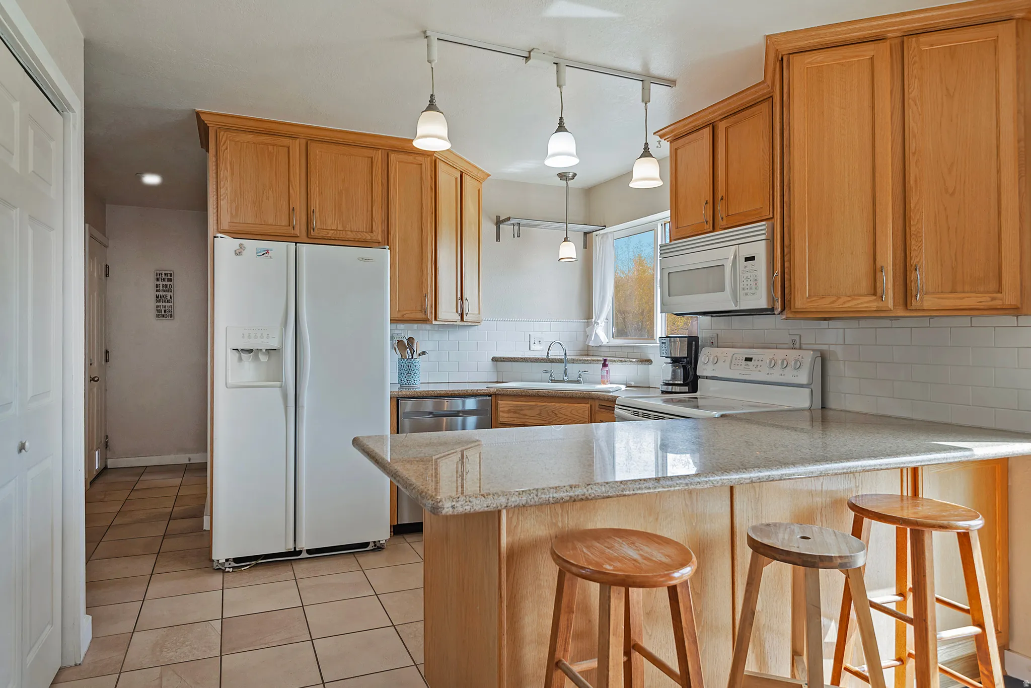 Kitchen with white appliances, a peninsula, a breakfast bar area, tasteful backsplash, and light tile patterned floors