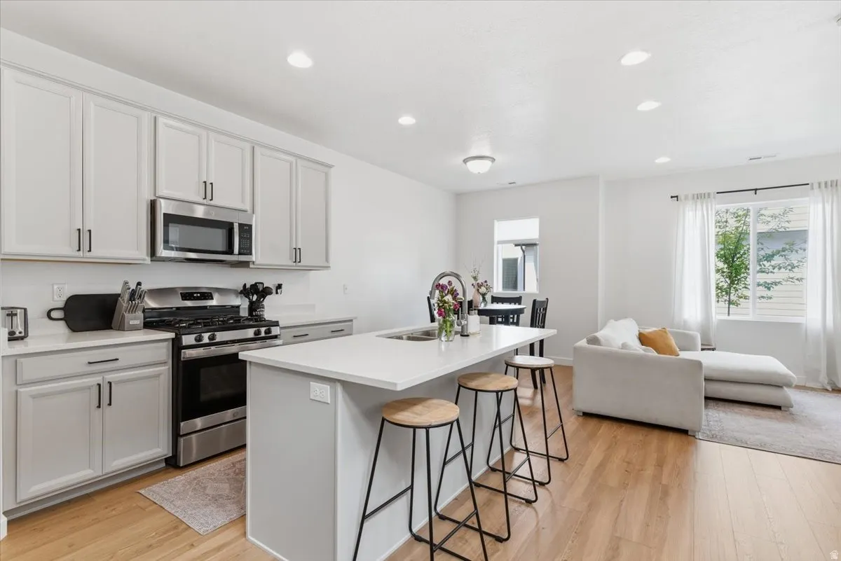 Kitchen featuring stainless steel appliances, a kitchen island with sink, light wood-style flooring, a kitchen breakfast bar, and recessed lighting