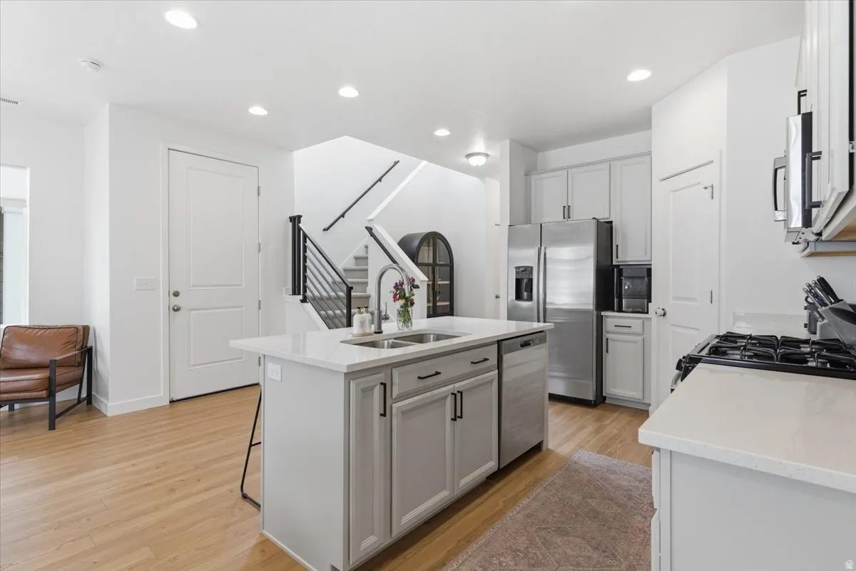 Kitchen featuring light stone countertops, light wood-style floors, a center island with sink, stainless steel appliances, and recessed lighting
