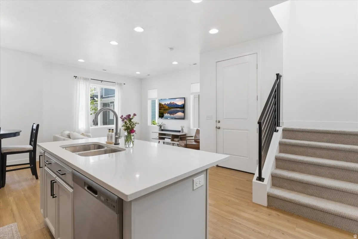 Kitchen featuring stainless steel dishwasher, a kitchen island with sink, recessed lighting, light stone countertops, and light wood finished floors