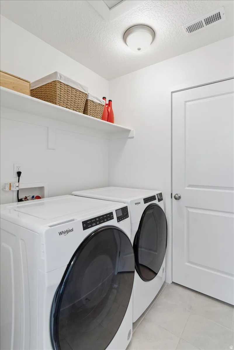 Laundry area with a textured ceiling, separate washer and dryer, and light tile patterned floors