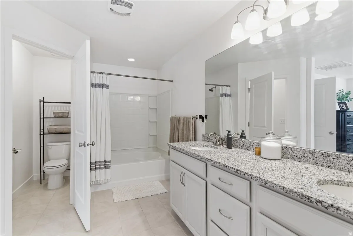 Full bathroom featuring double vanity, shower / bath combination with curtain, and light tile patterned floors