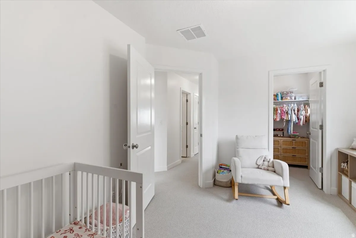Bedroom with a walk in closet, a nursery area, and light colored carpet