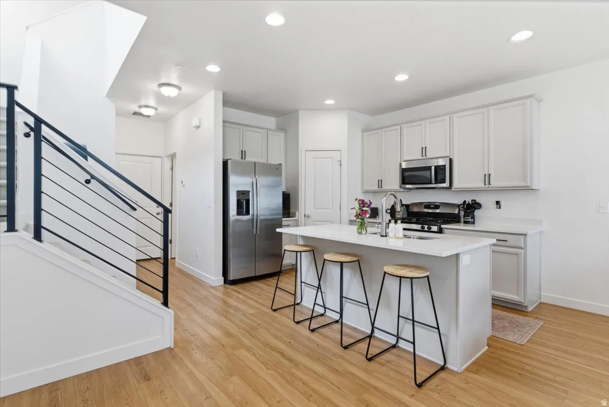 Kitchen with a kitchen bar, stainless steel appliances, a center island with sink, light wood-style flooring, and recessed lighting