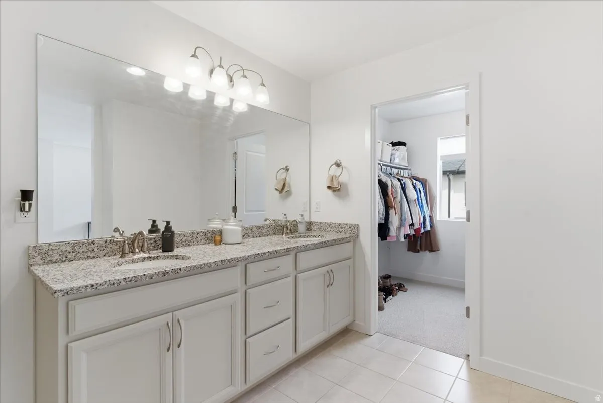 Full bathroom with double vanity, a walk in closet, and light tile patterned floors