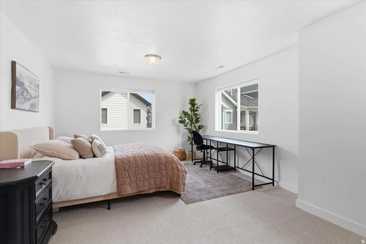 Bedroom featuring light carpet, multiple windows, and a textured ceiling