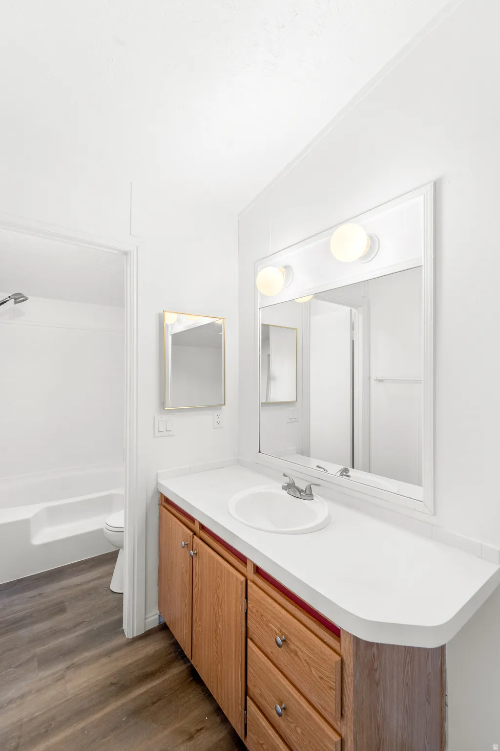 Bathroom with vanity, dark wood-style floors, vaulted ceiling, and tub / shower combination