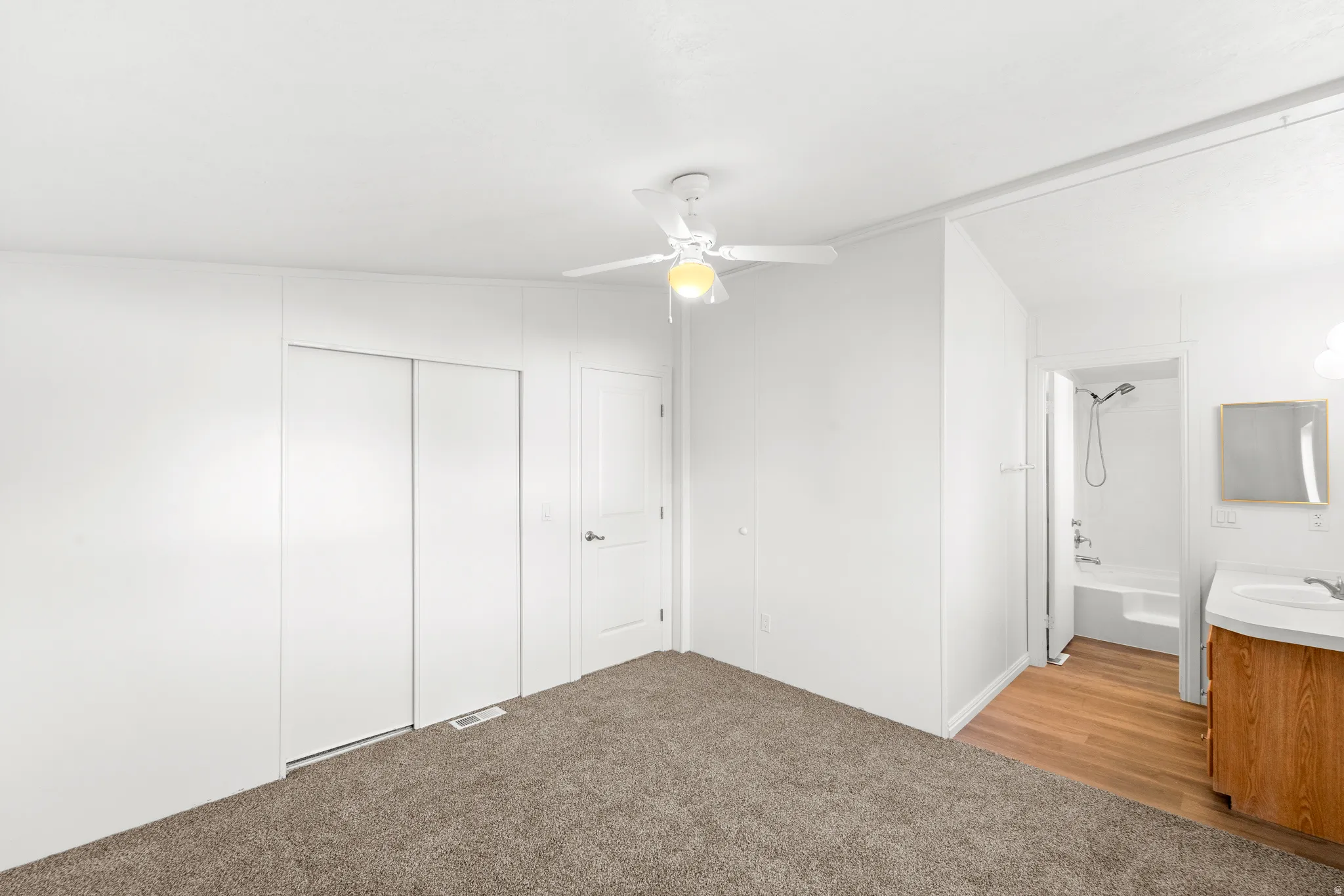 Unfurnished bedroom with light carpet, ceiling fan, a closet, and ensuite bath