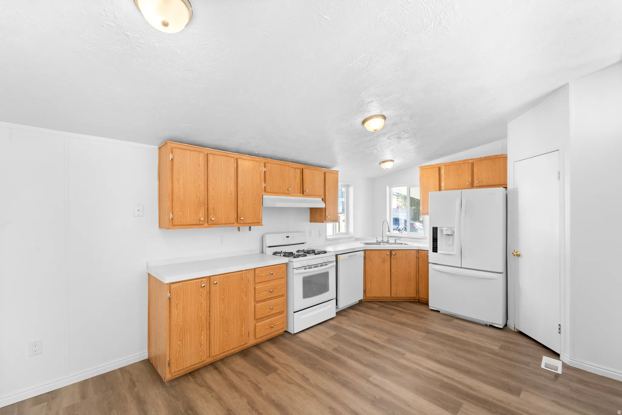 Kitchen with white appliances, light countertops, vaulted ceiling, light wood finished floors, and light wood finish cabinets