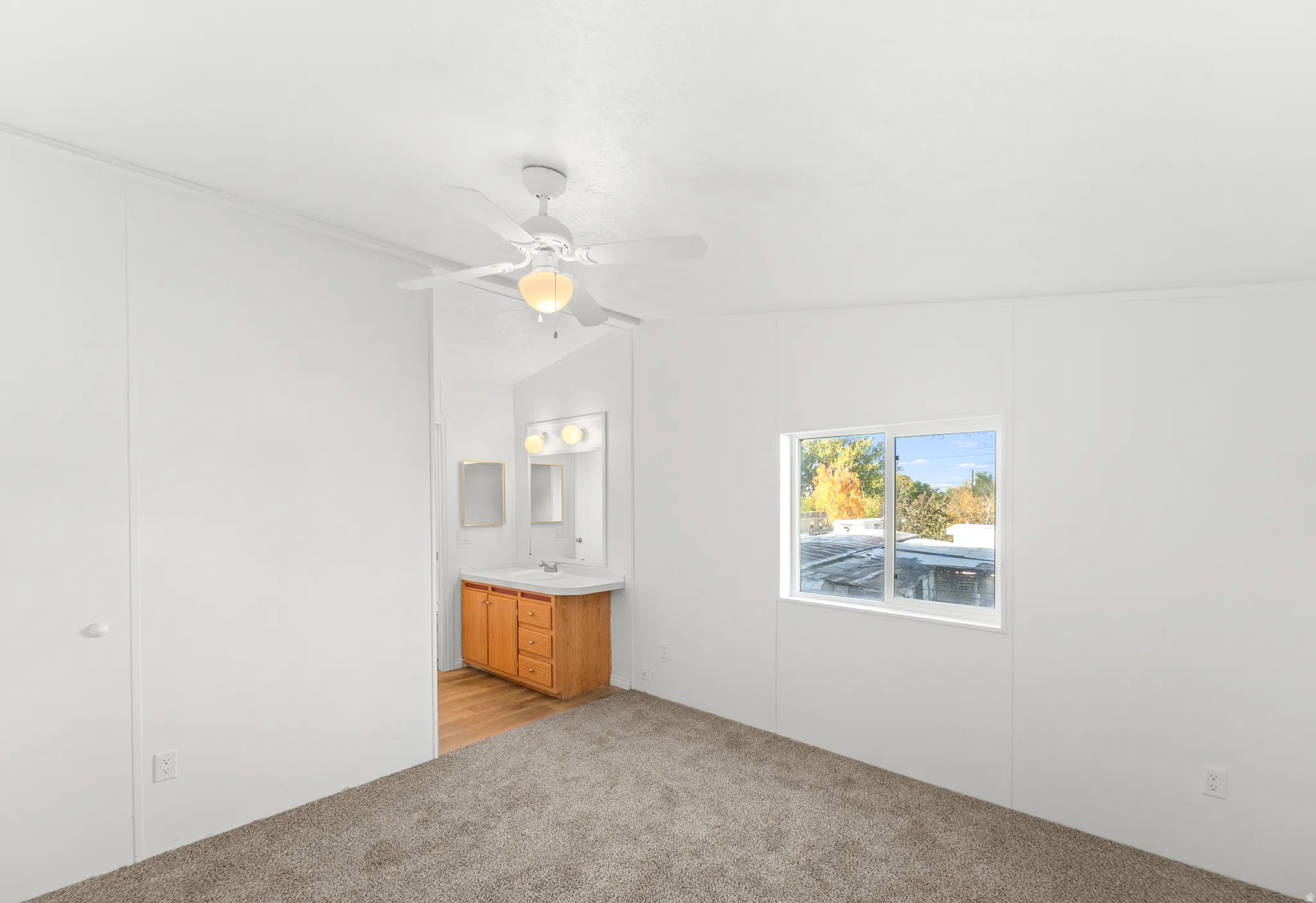 Unfurnished bedroom featuring light carpet, vaulted ceiling, ensuite bathroom, and a ceiling fan