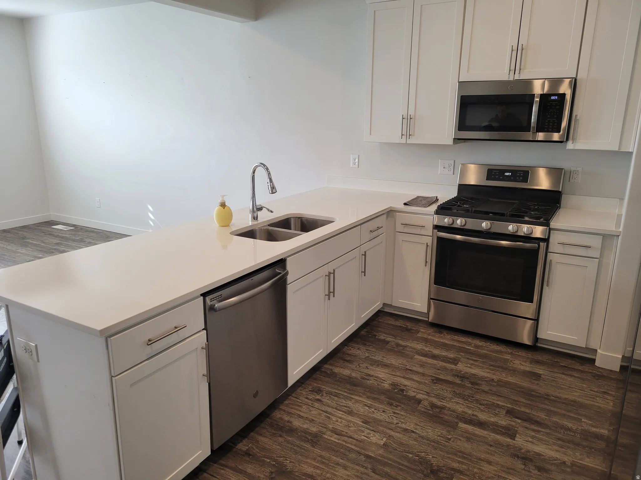 Kitchen featuring dark wood-style flooring, stainless steel appliances, a peninsula, white cabinetry, and light stone countertops