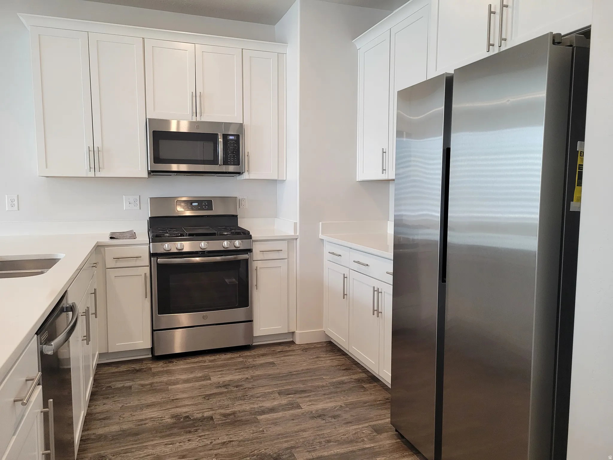 Kitchen featuring stainless steel appliances, dark wood-style floors, white cabinetry, and light stone counters