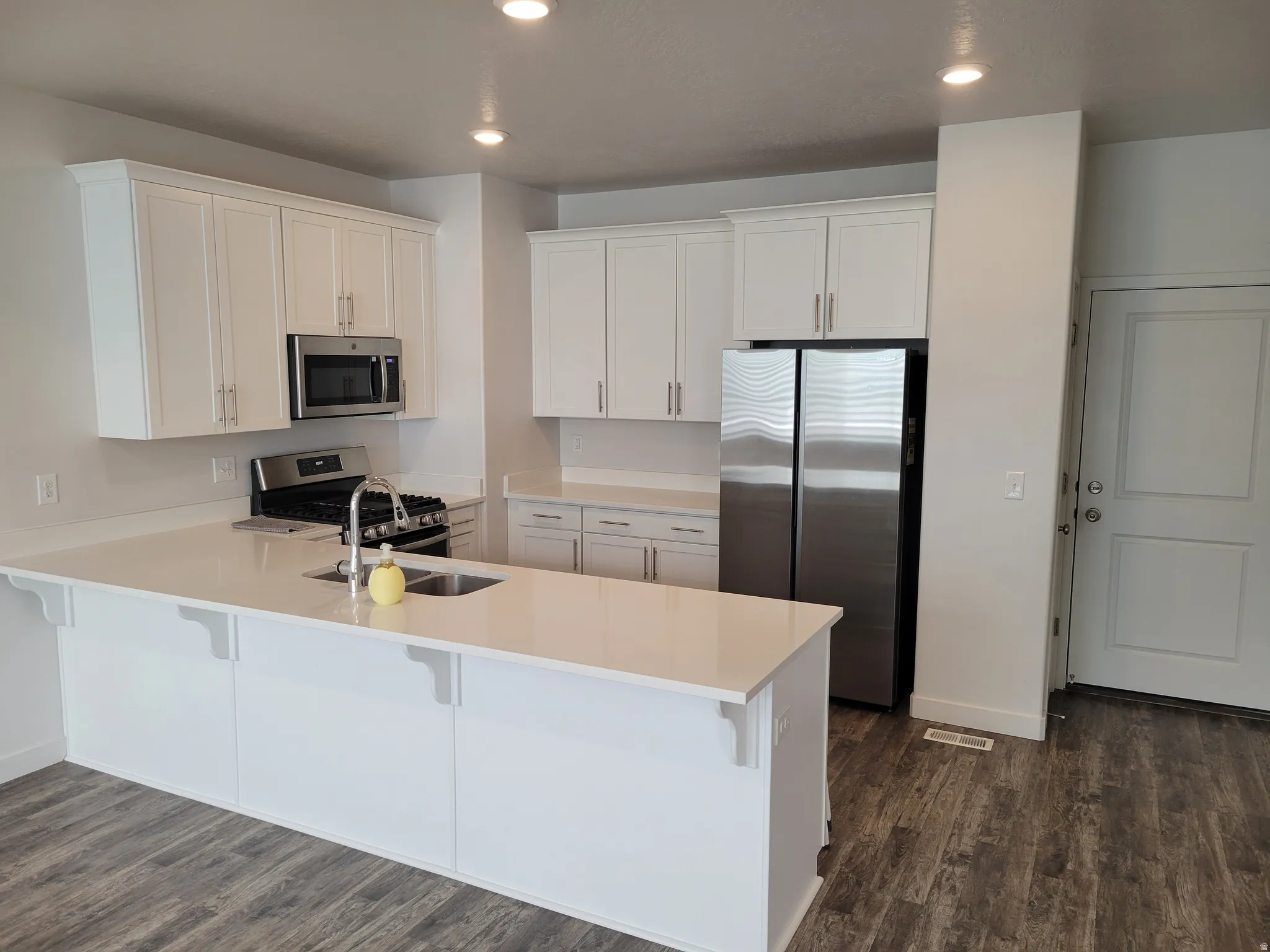 Kitchen with a peninsula, white cabinetry, stainless steel appliances, a kitchen breakfast bar, and dark wood-style flooring