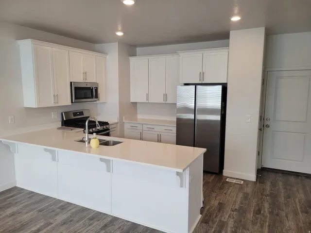 Kitchen with a peninsula, white cabinetry, stainless steel appliances, a kitchen breakfast bar, and dark wood-style flooring