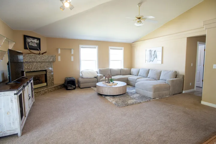 Living room with light carpet, a ceiling fan, a fireplace, and vaulted ceiling