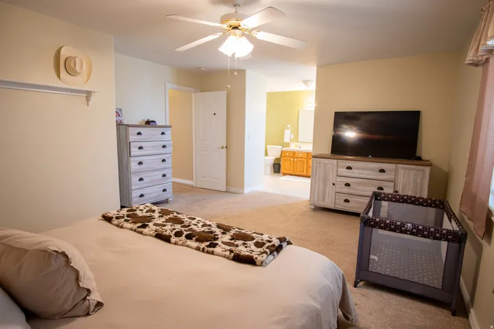 Bedroom featuring light colored carpet, a ceiling fan, and ensuite bath