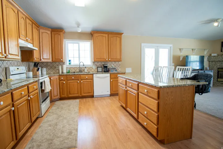 Kitchen with white appliances, light stone counters, and wood finish cabinets