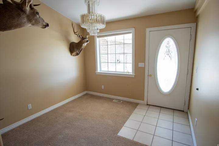 Foyer with light tile patterned floors, hanging lights, and light carpet