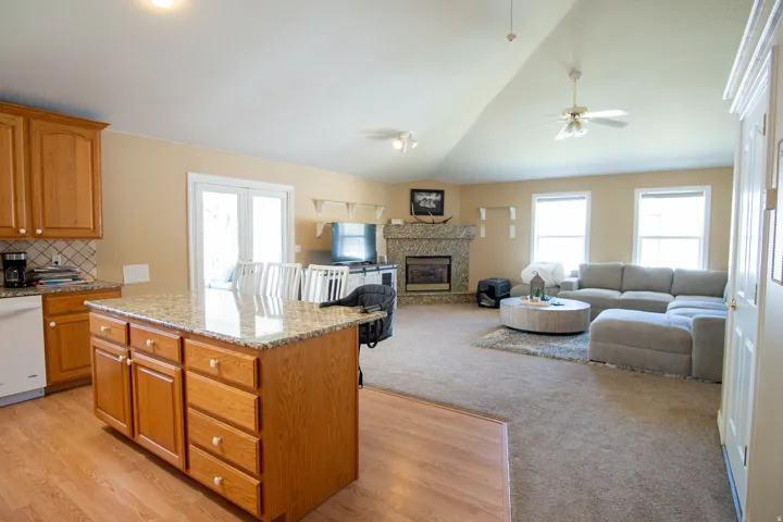 Kitchen with light stone countertops, a kitchen island, open floor plan, dishwasher, and wood finish cabinets