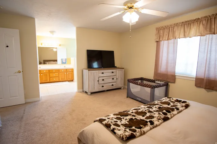 Bedroom featuring light carpet, connected bathroom, and a ceiling fan