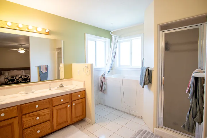 Bathroom with connected bathroom, double vanity, a shower stall, light tile patterned floors, and a garden tub