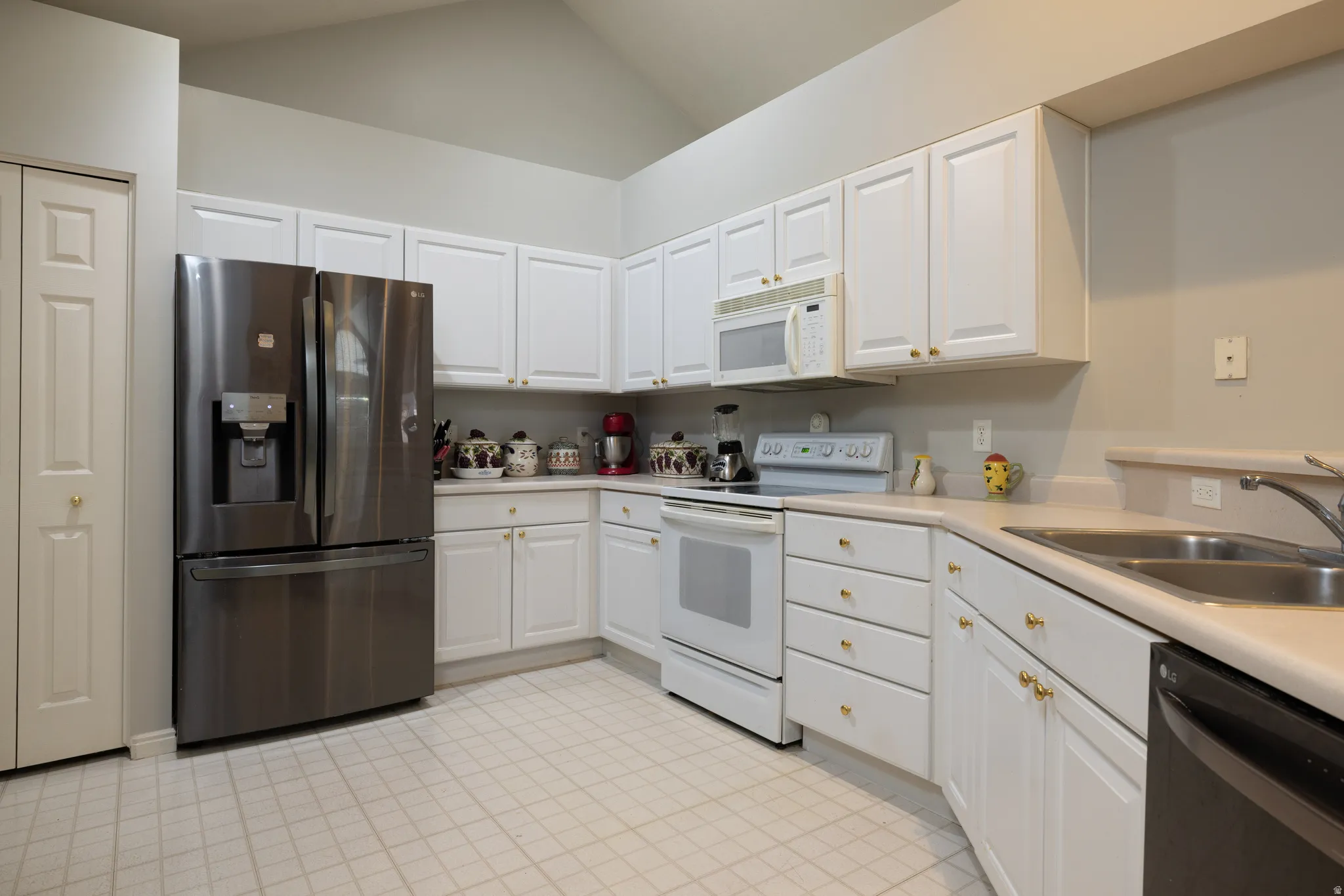 Kitchen with white appliances, lofted ceiling, and white cabinetry